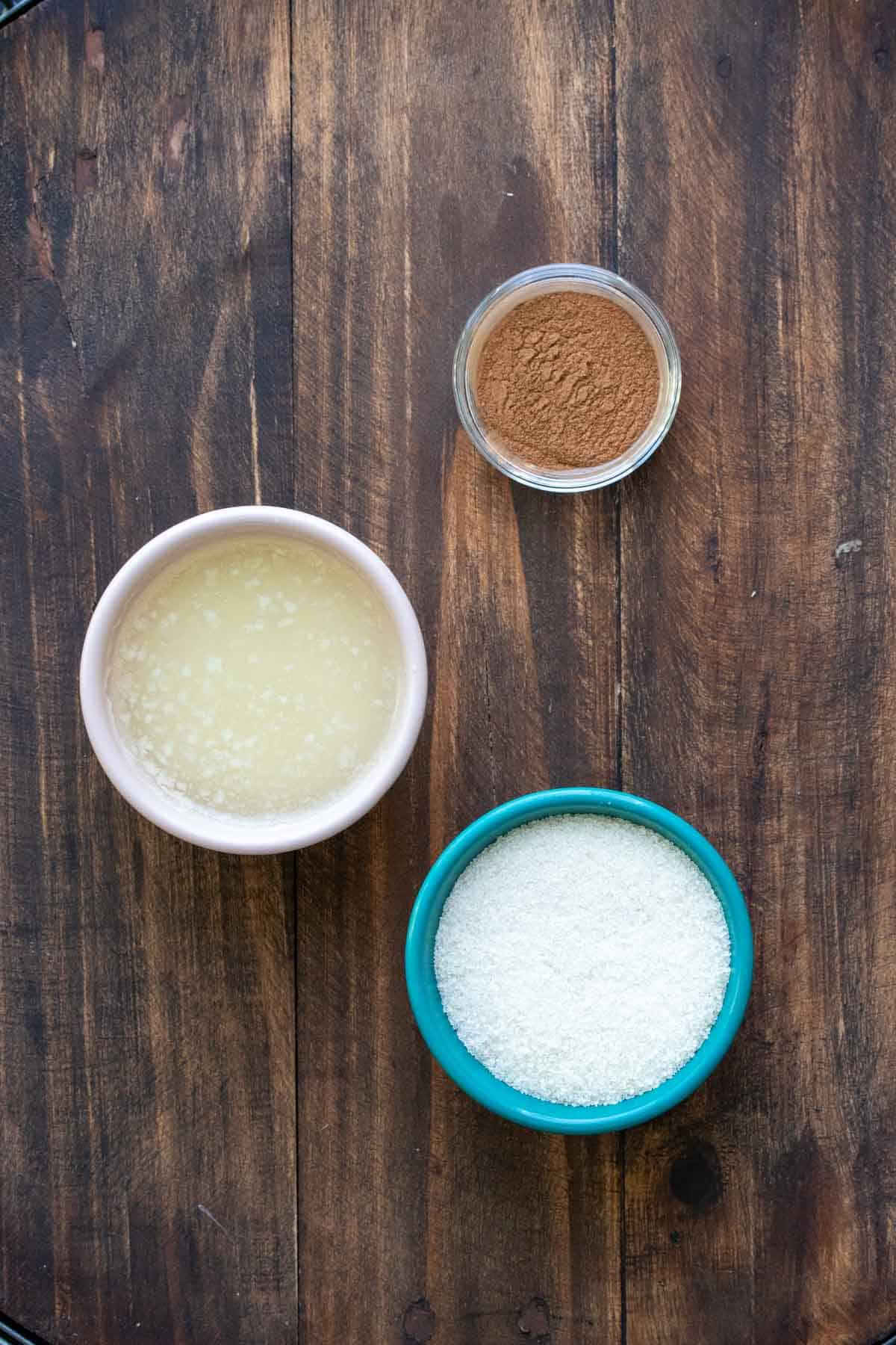 Bowls of sugar, butter and cinnamon on a wooden surface