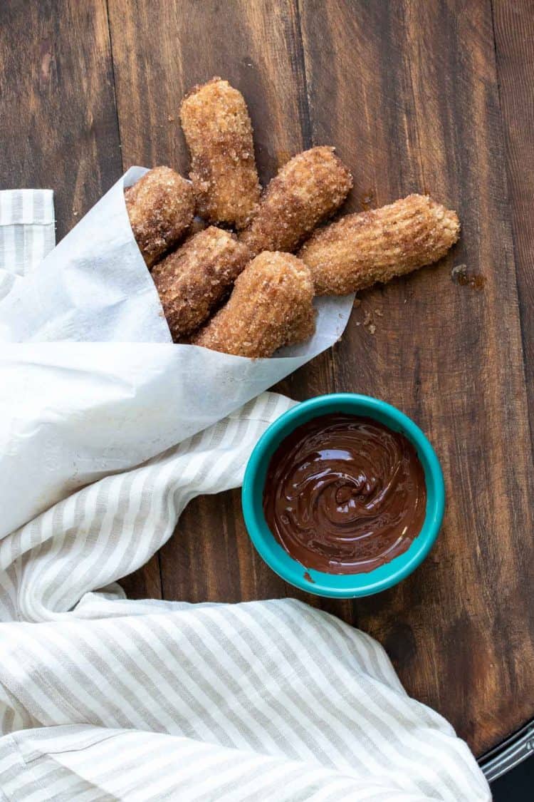 Churro pieces wrapped in a parchment cone next to a bowl of chocolate