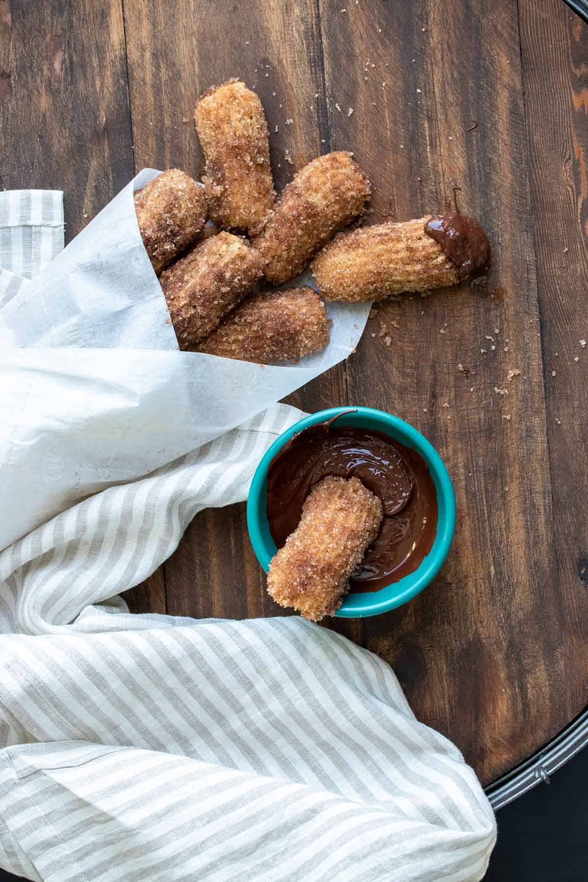 Churro dipping in a bowl of chocolate next to a pile of more churros