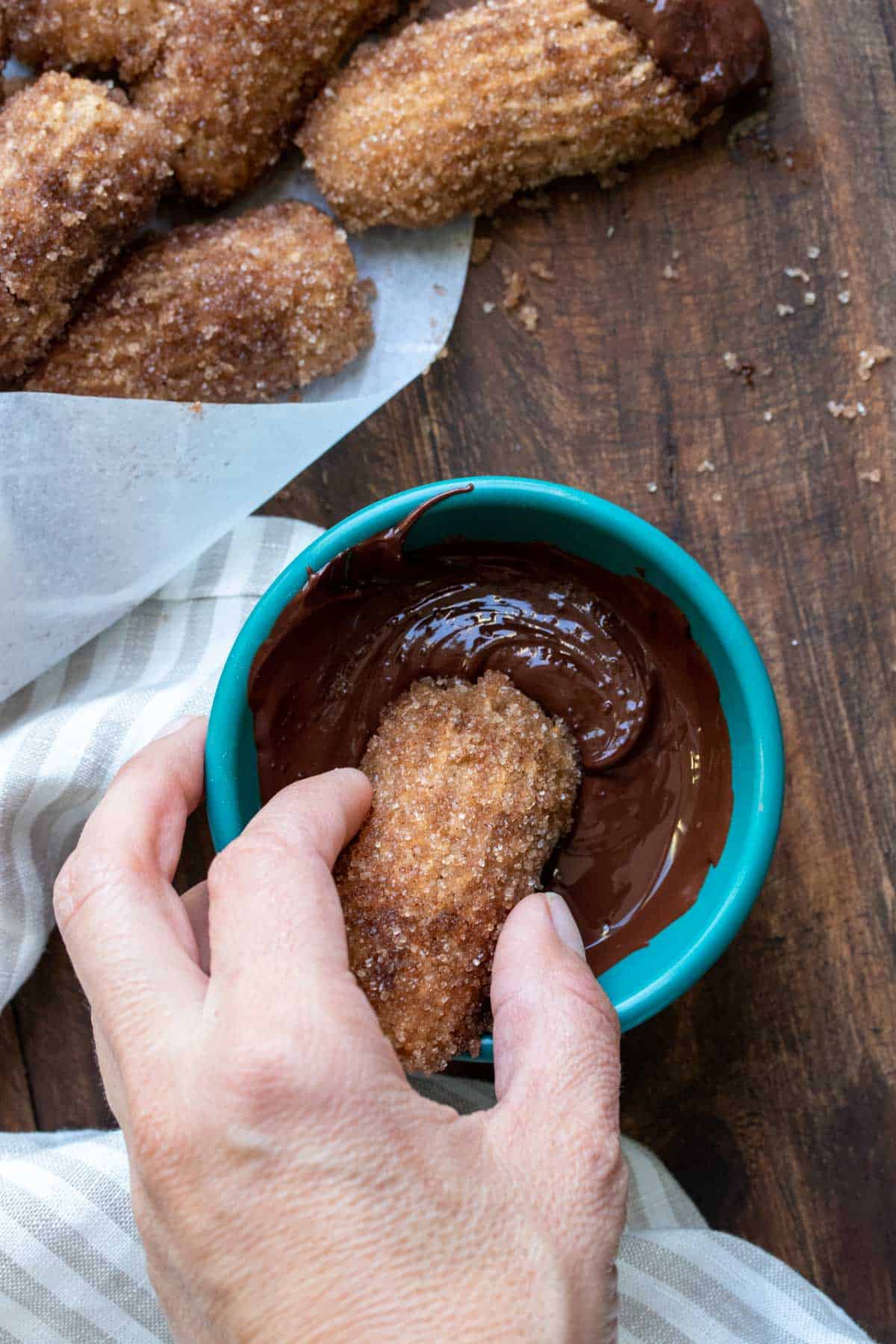 Hand dipping a churro piece in a bowl of melted chocolate