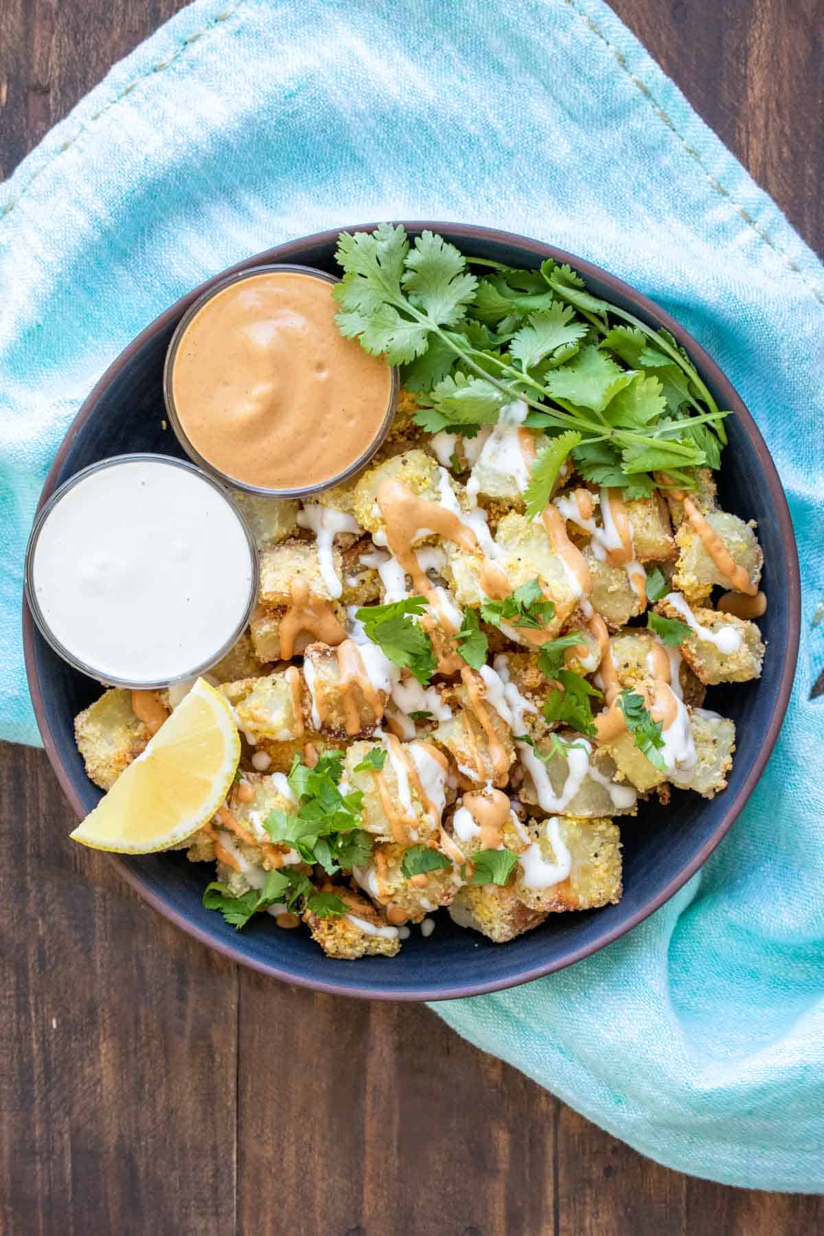 Cubed crispy potatoes piled in a dark blue bowl and drizzled with sauce