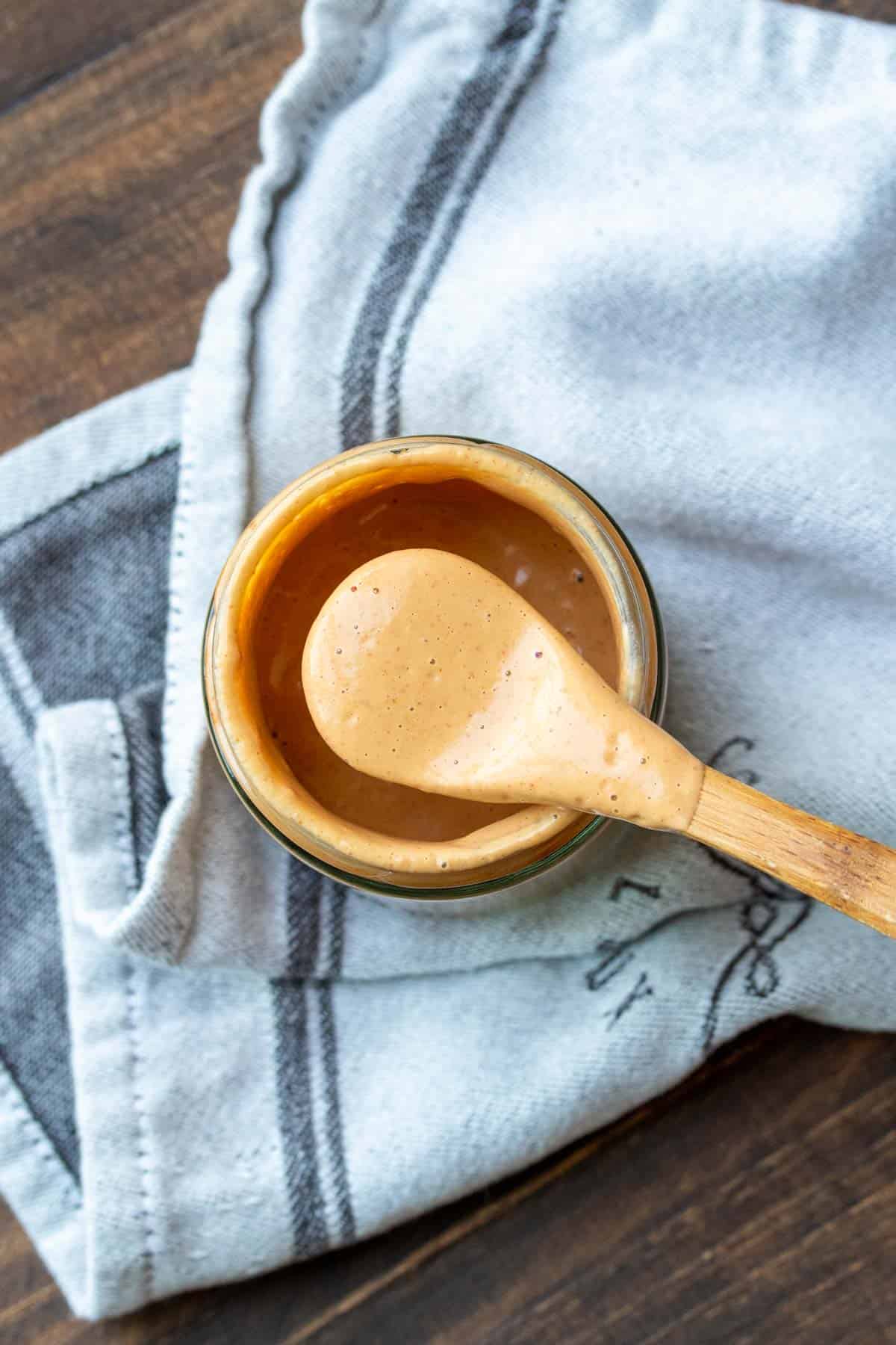 Wooden spoon taking a spoonful of creamy orange colored sauce from a jar