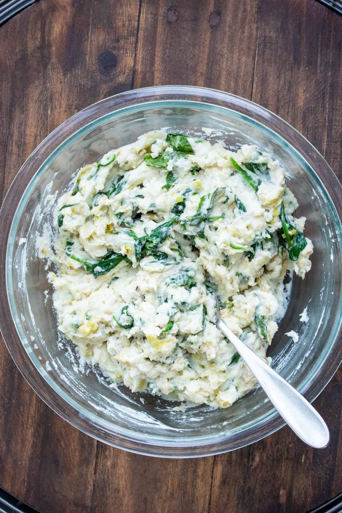 Glass bowl filled with mashed potatoes and sauteed greens mixed together.