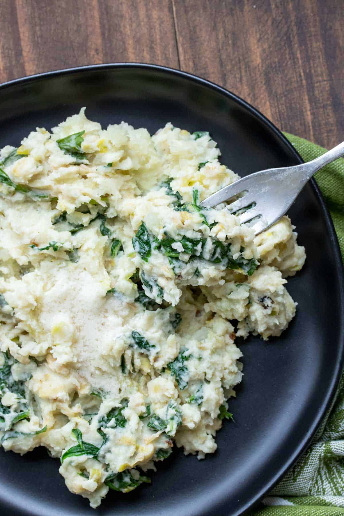 Fork getting a bite of colcannon from a black plate.