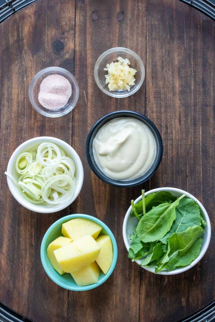 Bowls on a wooden surface filled with ingredients to make a mashed potatoes dish with greens