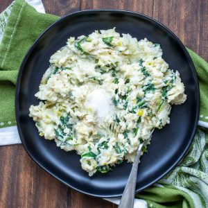 Irish mashed potatoes and greens on a black plate with a fork in it.