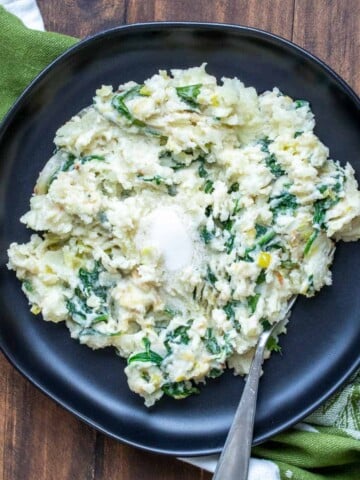 Irish mashed potatoes and greens on a black plate with a fork in it.