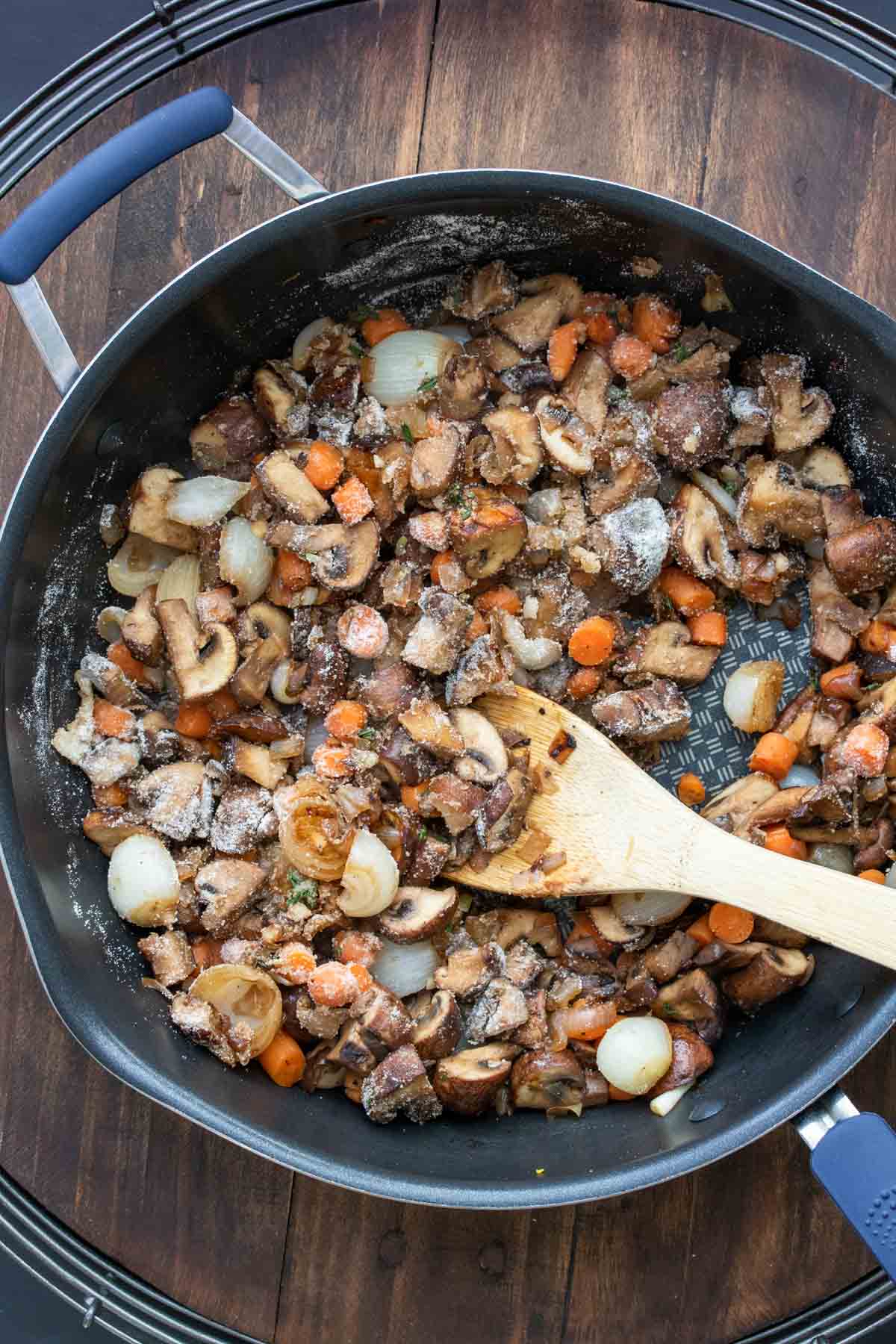 Wooden spoon mixing a mushroom mixture in a pan as it cooks