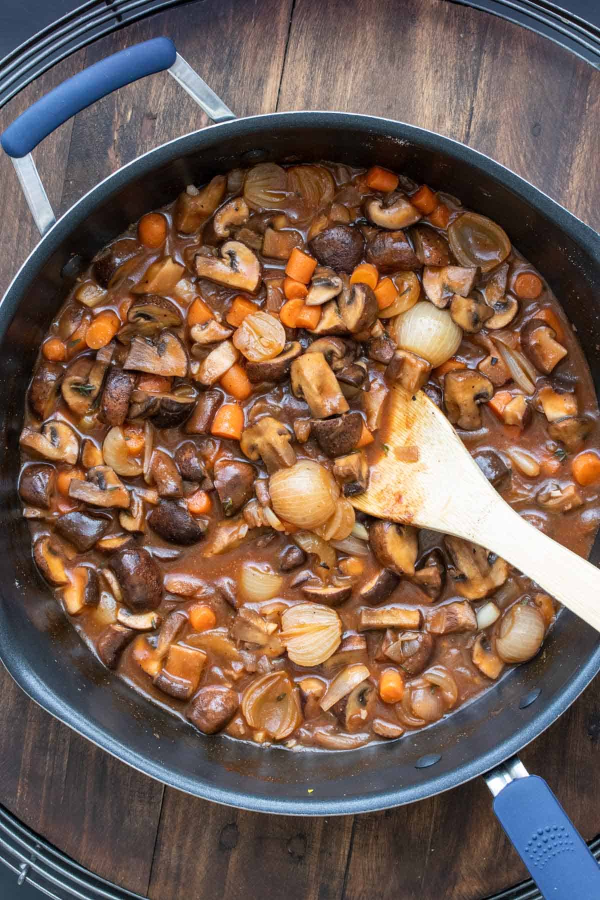 Thick broth based mixture with carrots, mushrooms and onions cooking in a pan