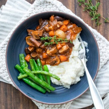 A blue bowl with mushroom bourguignon, mashed potatoes and green beans