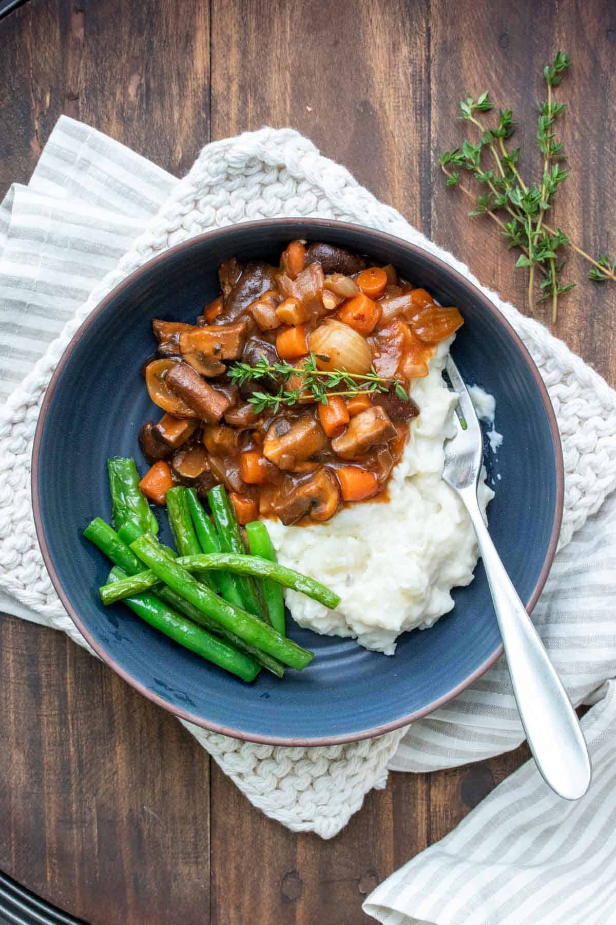 A blue bowl with mushroom bourguignon, mashed potatoes and green beans