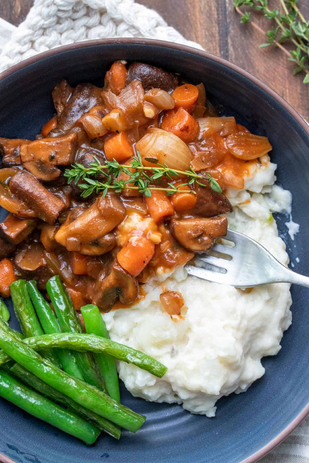 Fork getting a bite of mushroom bourguignon and mashed potatoes from a blue bowl