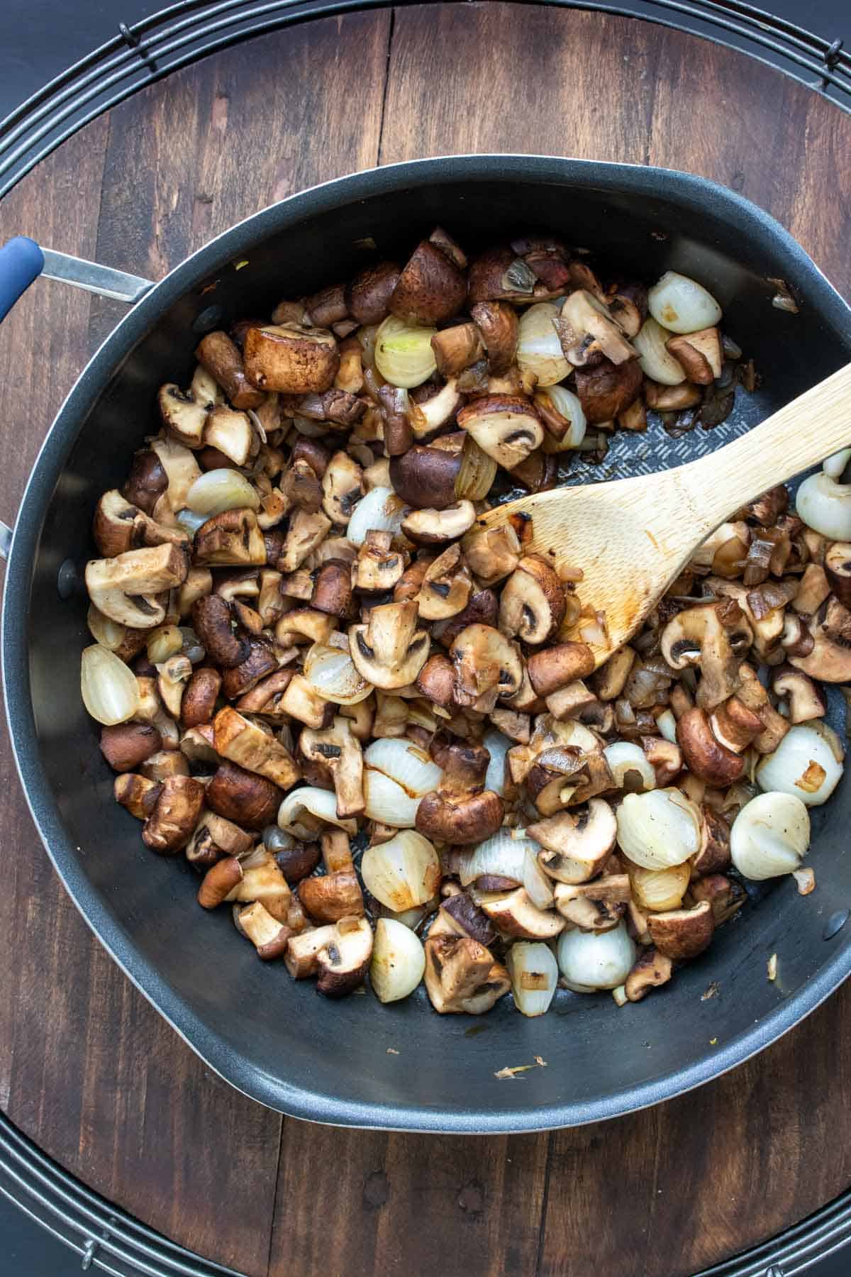 Wooden spoon mixing pearl onions and mushrooms in a pan