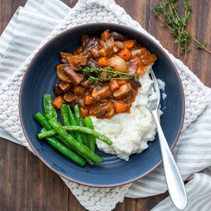 Mushroom bourguignon on top of mashed potatoes and green beans in a blue bowl