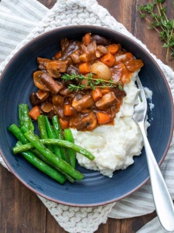 Mushroom bourguignon on top of mashed potatoes and green beans in a blue bowl