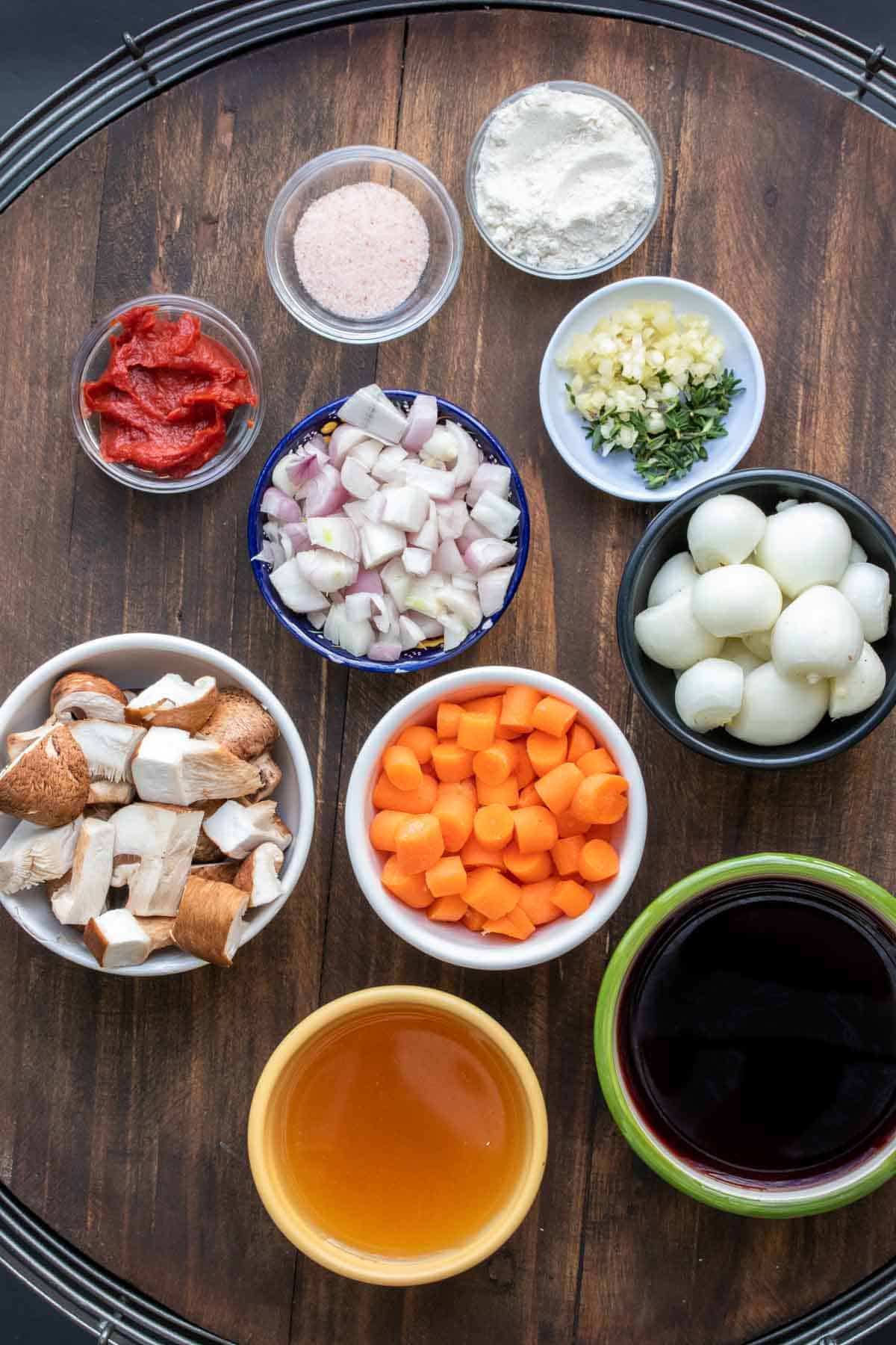 Different colored bowls on a wooden surface filled with ingredients to make mushroom bourguignon