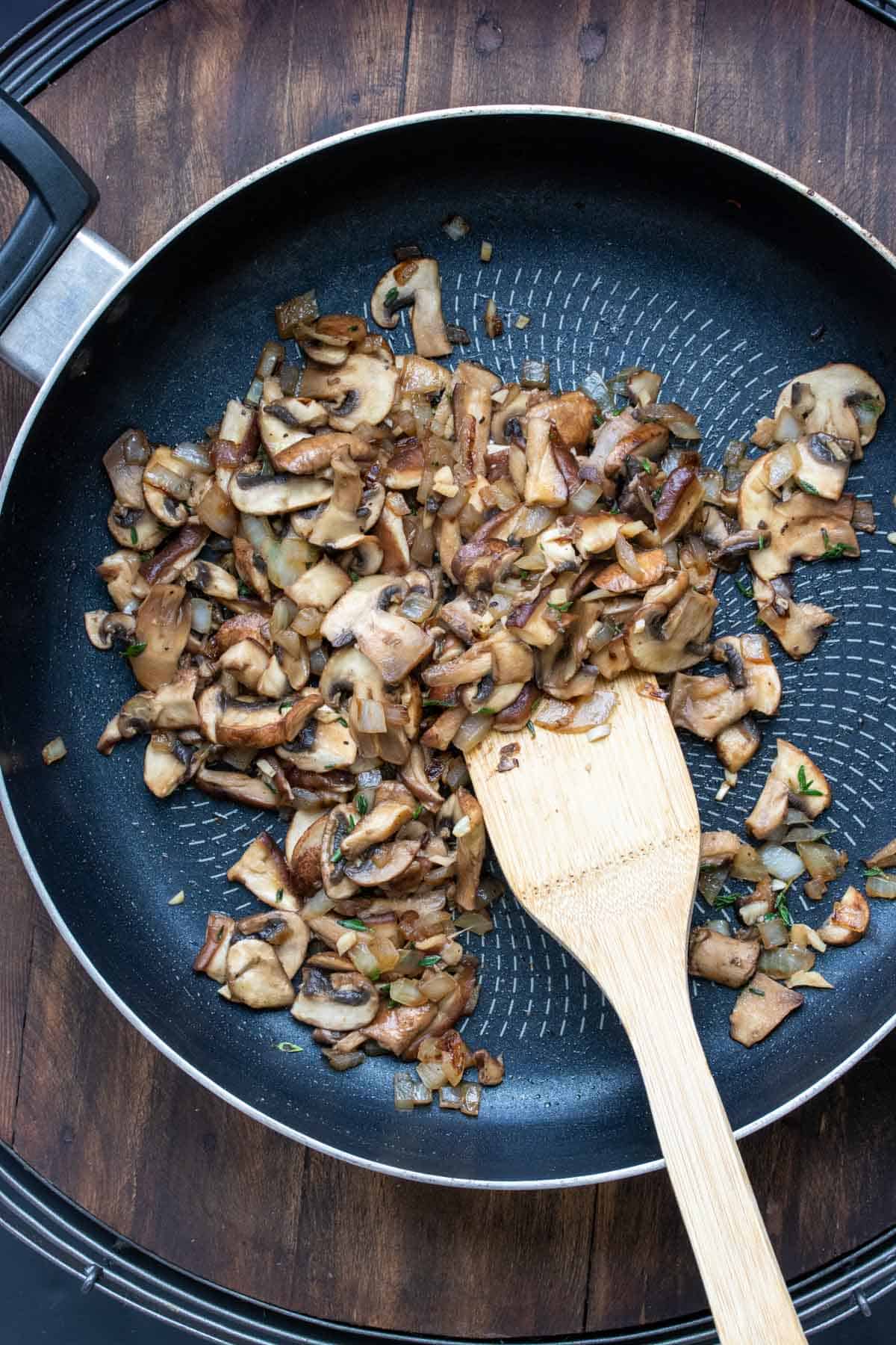 Wooden spatula mixing mushrooms in a pan to brown them.