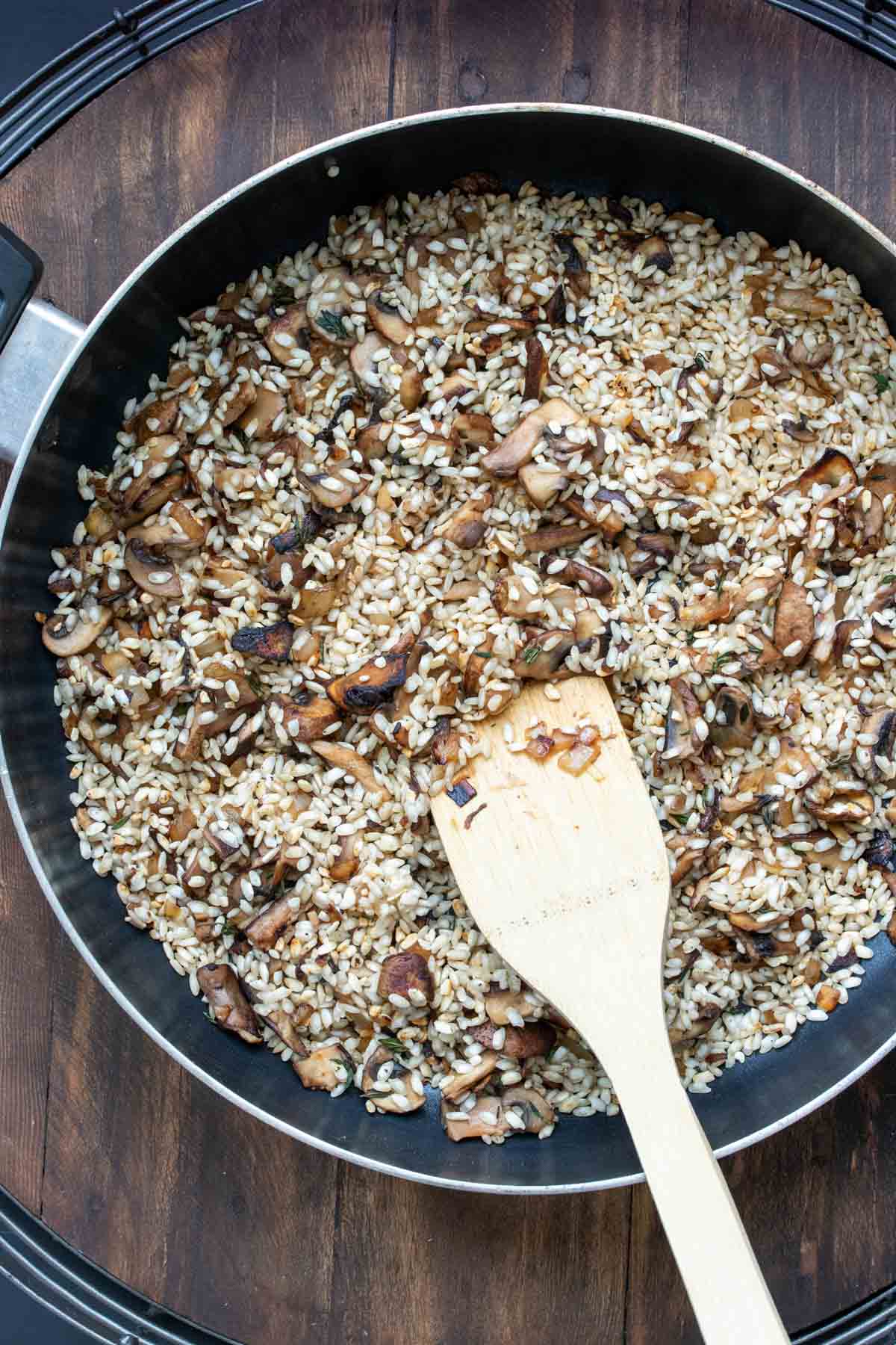 Pan filled with mushrooms and uncooked rice being browned.