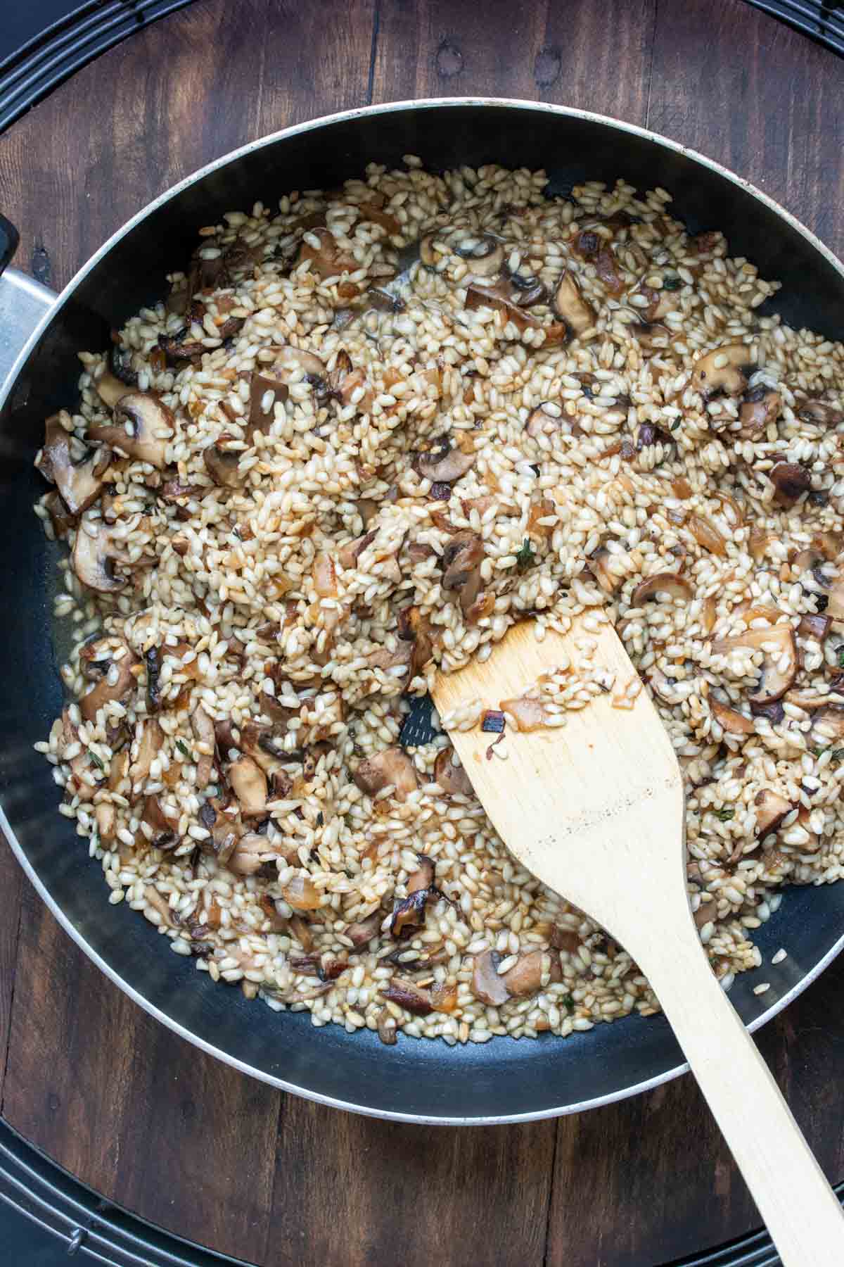 Mushrooms cooking with rice and broth in a pan and being stirred by a wooden spatula.