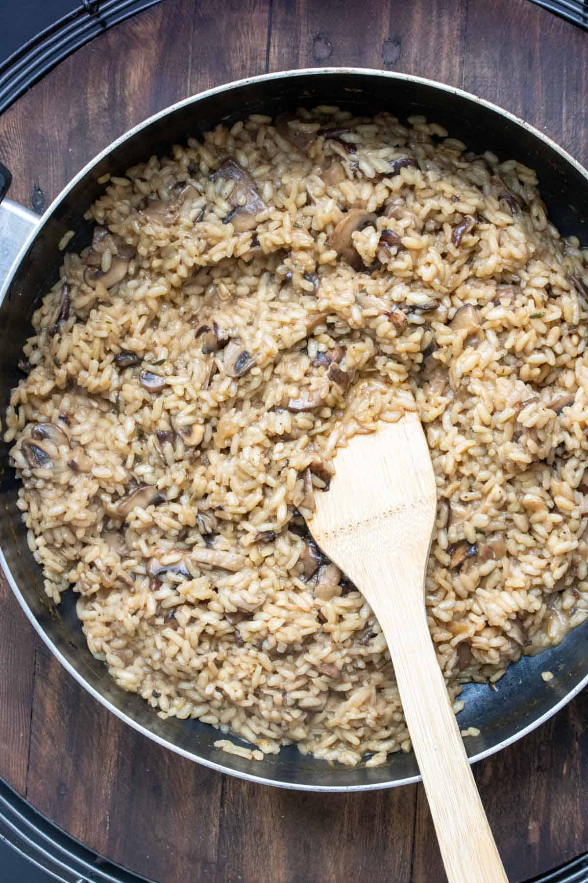 Pan with mushroom risotto cooking inside being stirred by a wooden spatula.