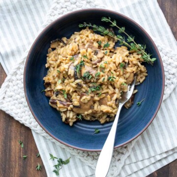 Dark blue bowl filled with mushroom risotto and topped with thyme