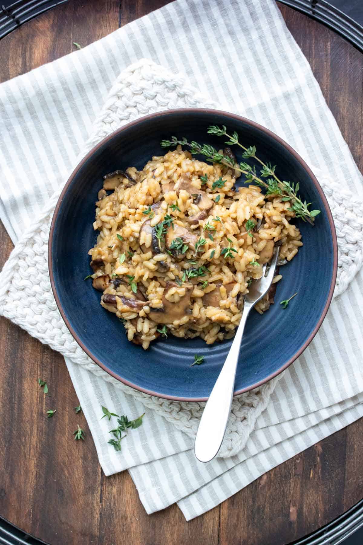 Dark blue bowl filled with mushroom risotto and topped with thyme.