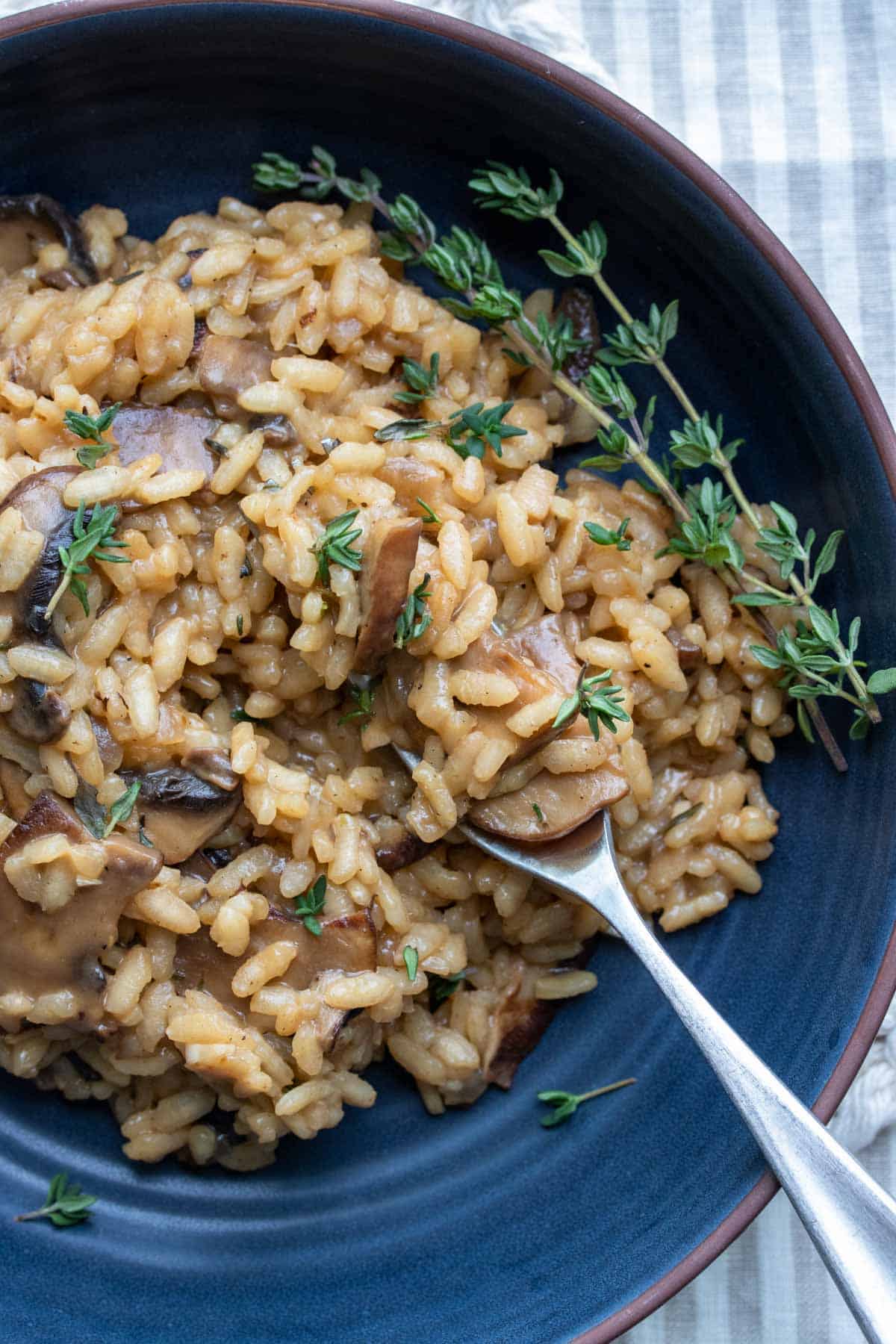 Fork getting a bite of mushroom risotto from a dark blue bowl.