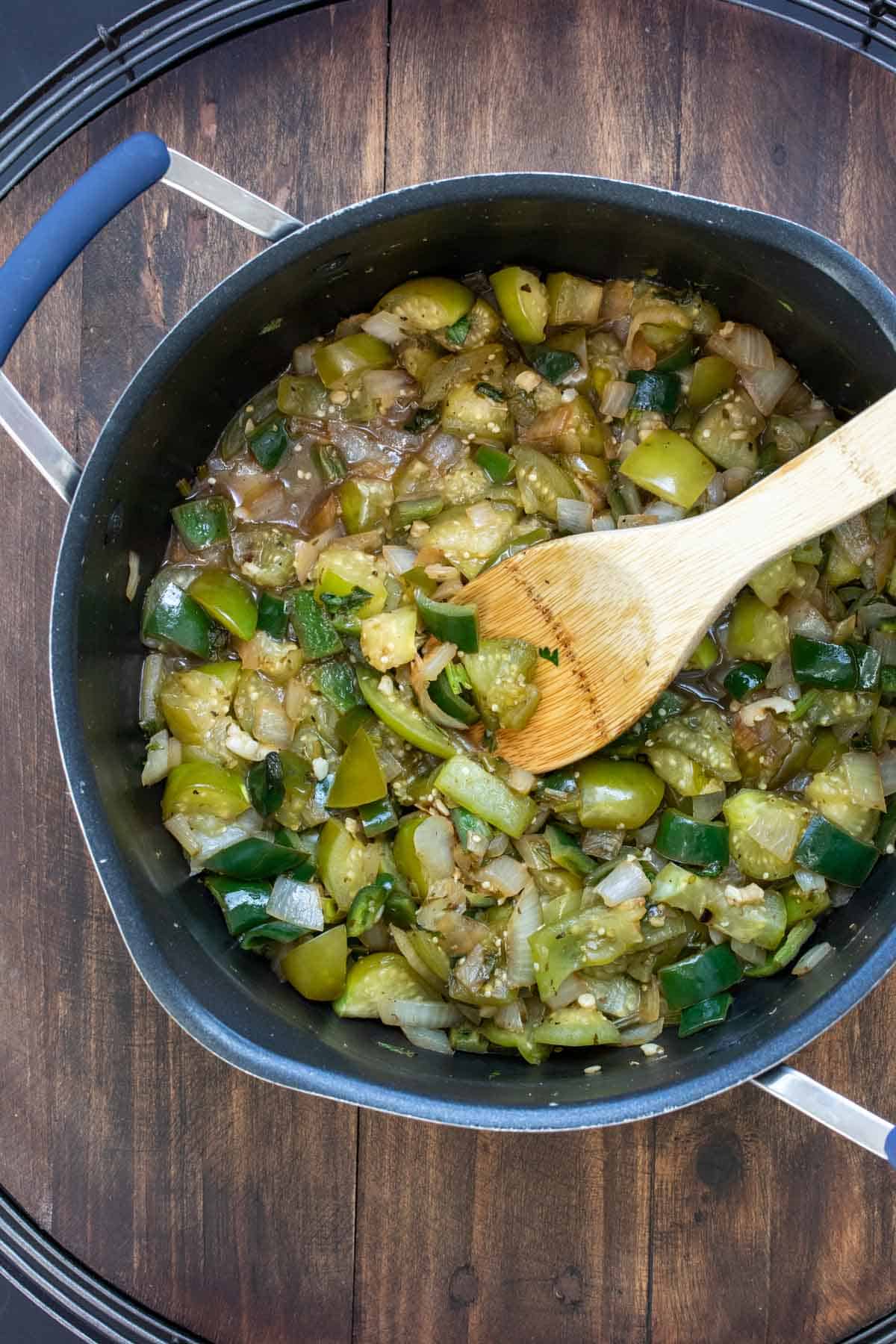 Wooden spoon mixing chopped tomatillos, peppers and cilantro in a pot.