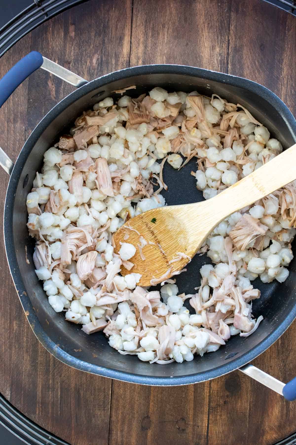 Wooden spoon mixing jackfruit and hominy in a pot