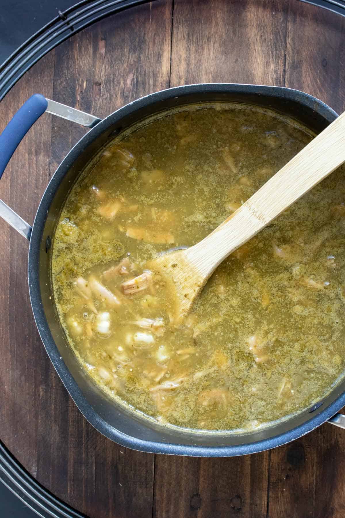 Wooden spoon mixing a green broth soup with jackfruit in it.