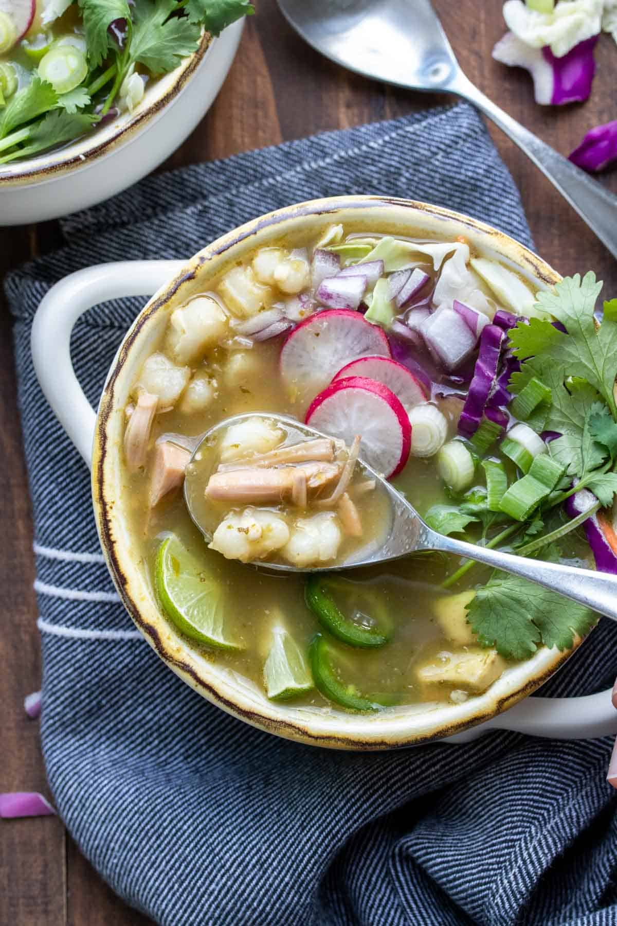 Spoon getting a bite of pozole verde soup from a bowl.