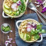 Pozole verde soup in soup bowls topped with cabbage, radishes, jalapeños cilantro and lime.