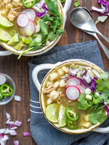 Pozole verde soup in soup bowls topped with cabbage, radishes, jalapeños cilantro and lime.