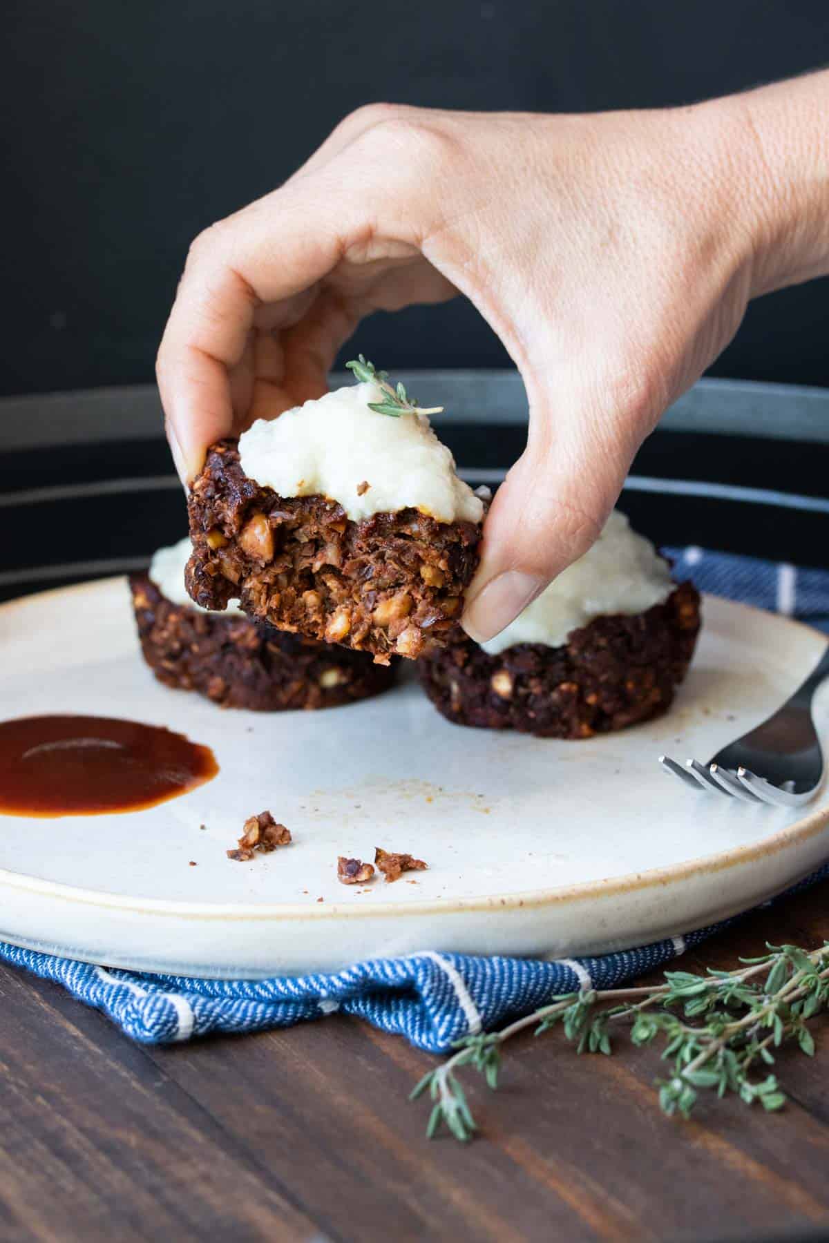 Lentil meatloaf cups on a plate and a hand picking up one