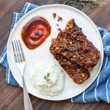 A white plate with slices of lentil meatloaf and mashed cauliflower with a scoop of sauce