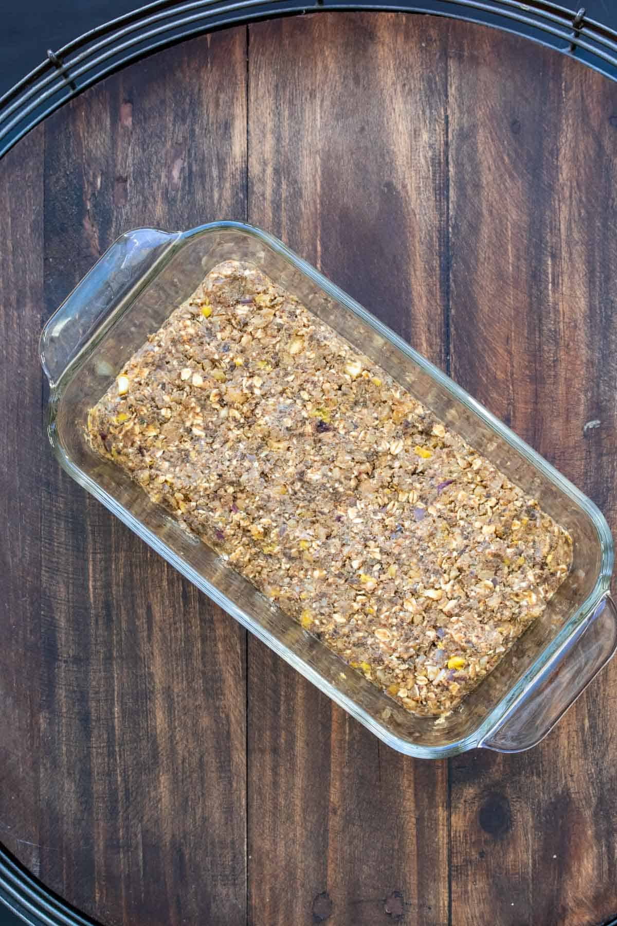 A glass loaf pan with raw lentil meatloaf mix.