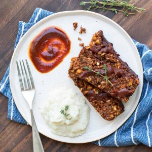 Sliced lentil meatloaf on a white plate with mashed cauliflower and barbecue sauce.