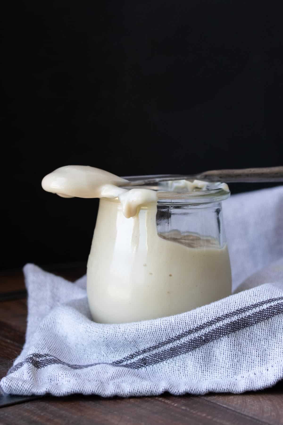 Silver knife laying on top of a glass jar filled with cream cheese frosting