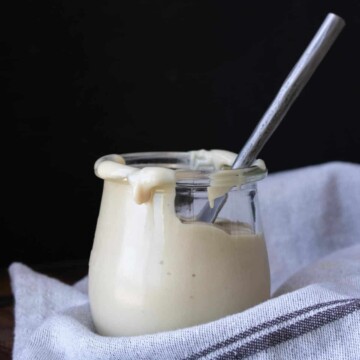 A glass jar with cream cheese frosting and a silver knife inside