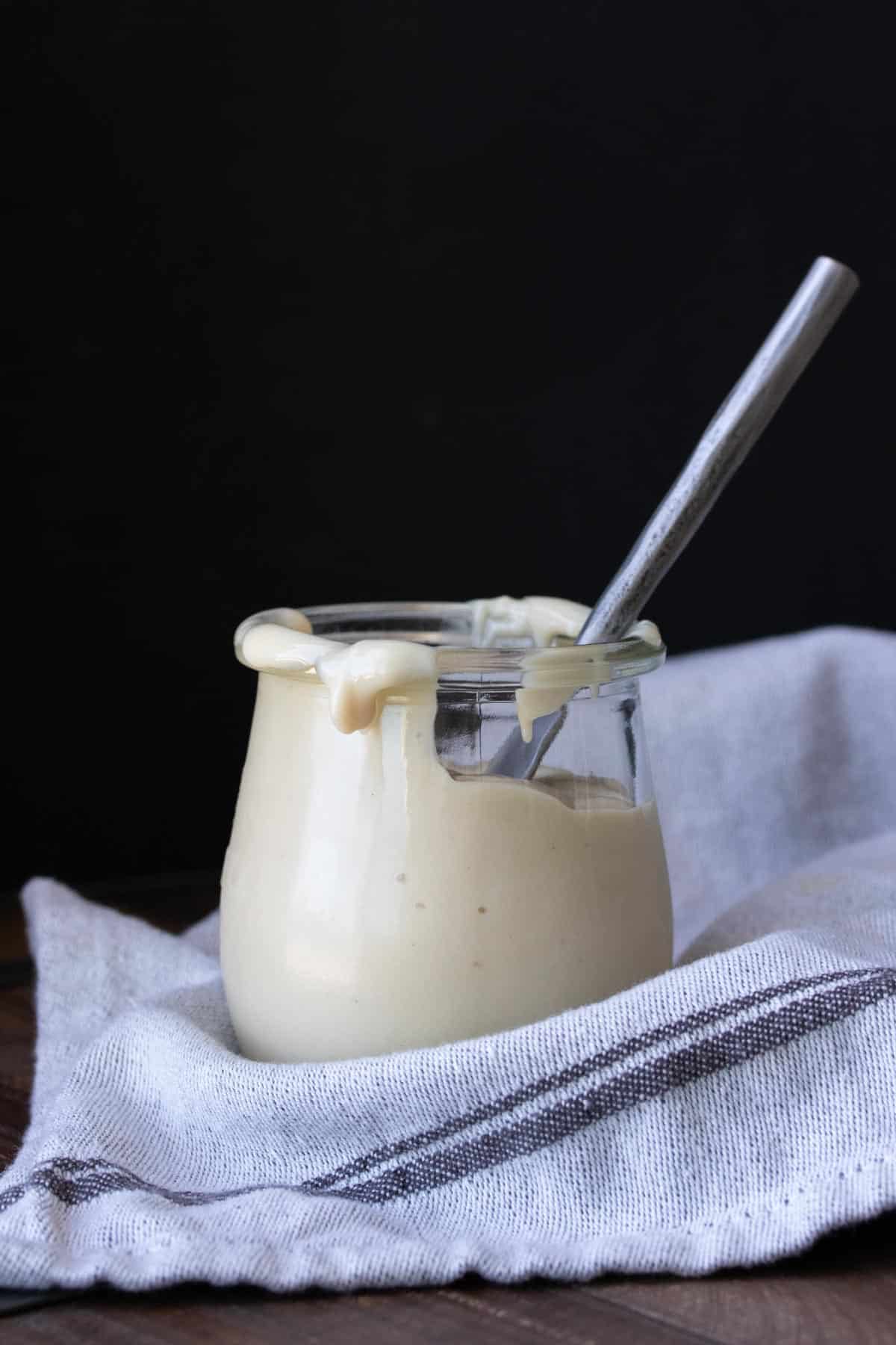 A glass jar with cream cheese frosting and a silver knife inside