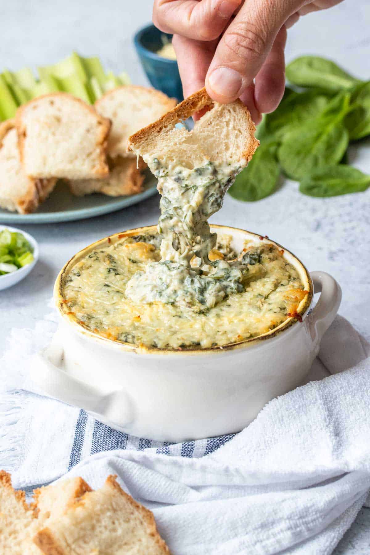 Hand dipping carrot piece in spinach artichoke dip