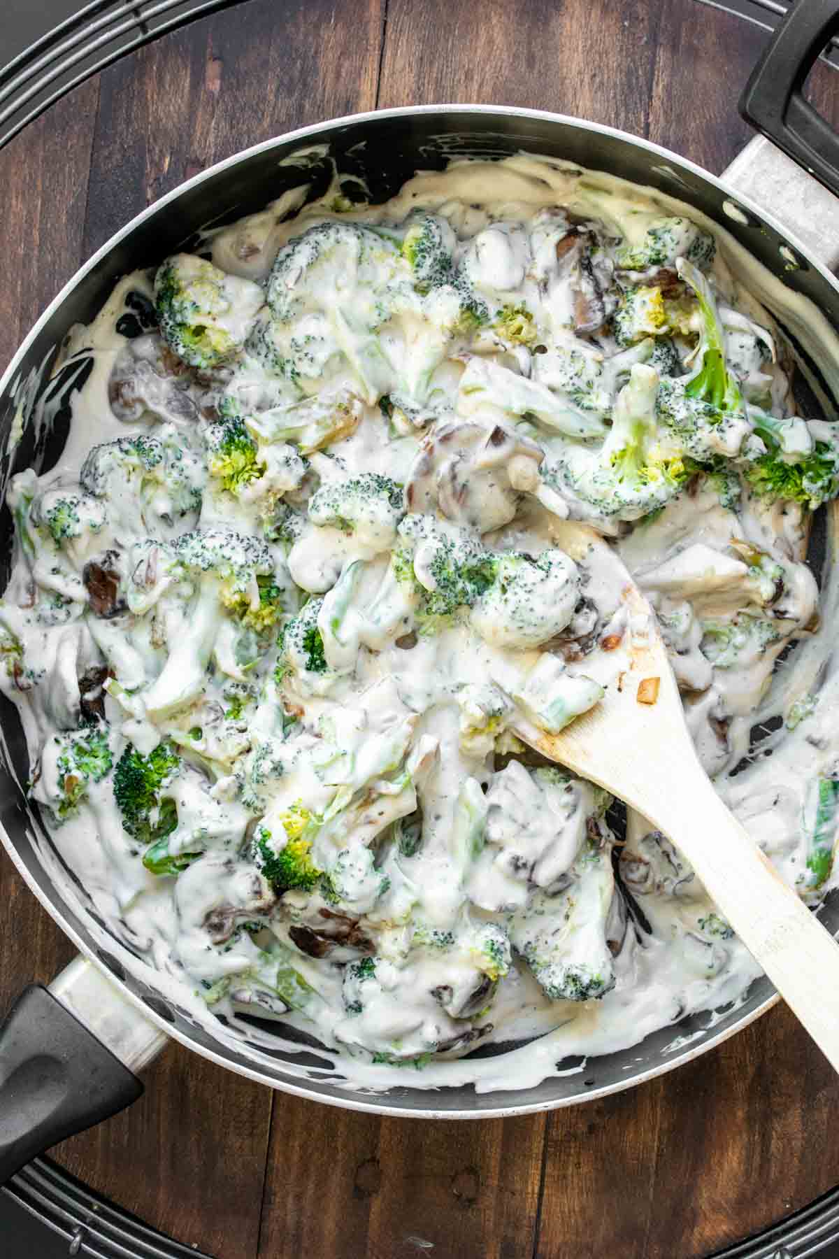 Wooden spoon mixing creamy broccoli in a pan.