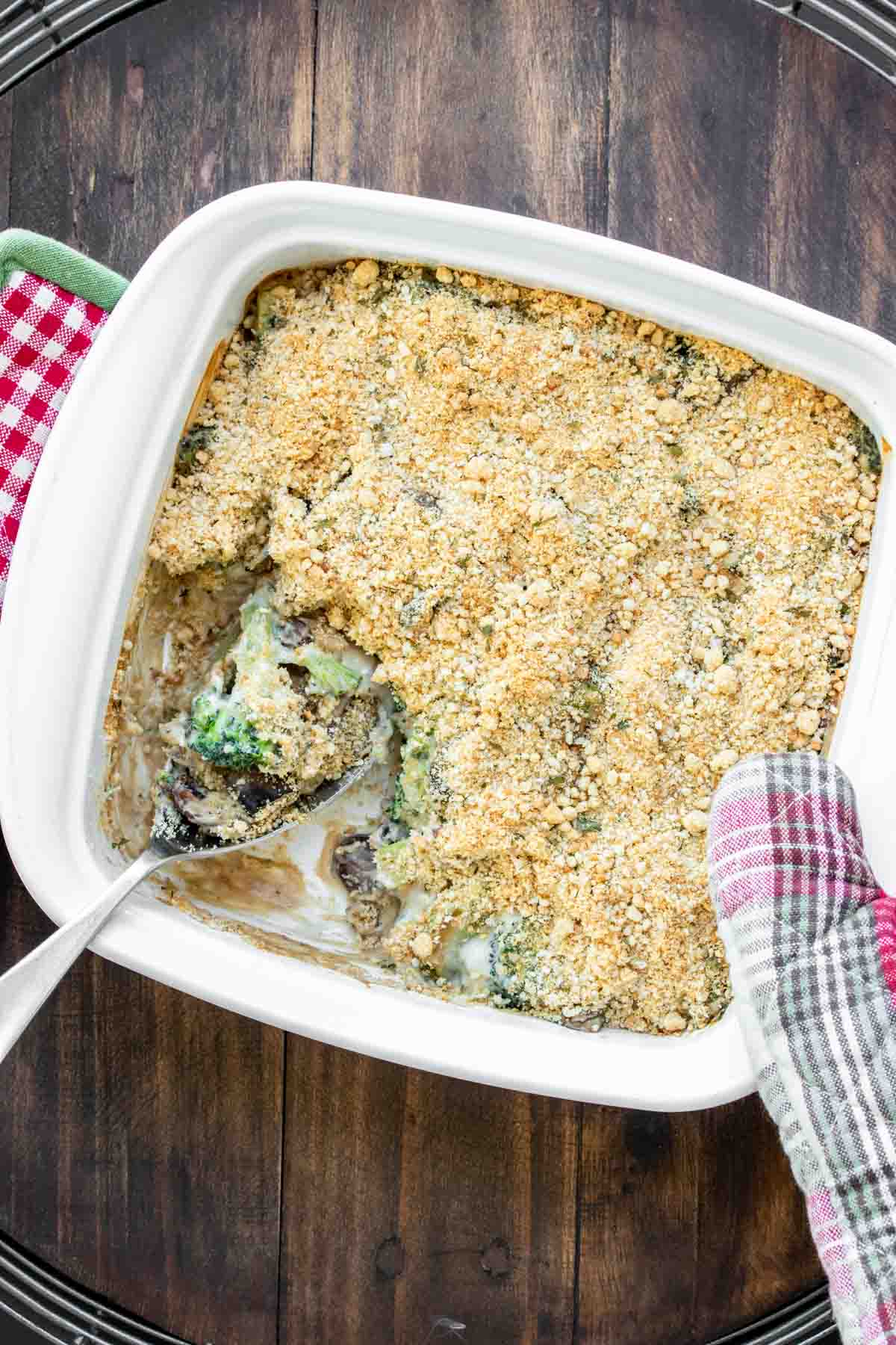 Oven mitt holding a white casserole dish with baked broccoli casserole.