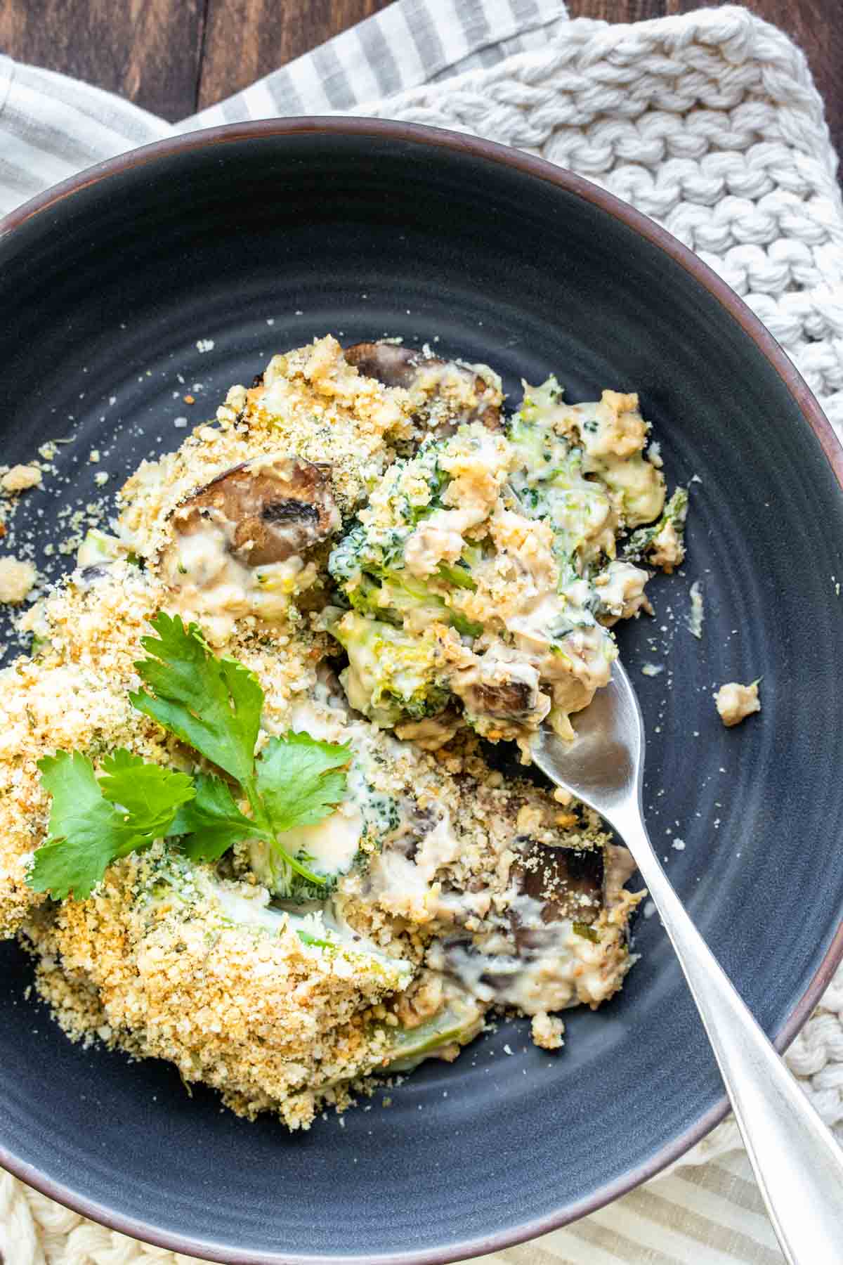 A fork getting a bite of broccoli casserole from a blue plate.