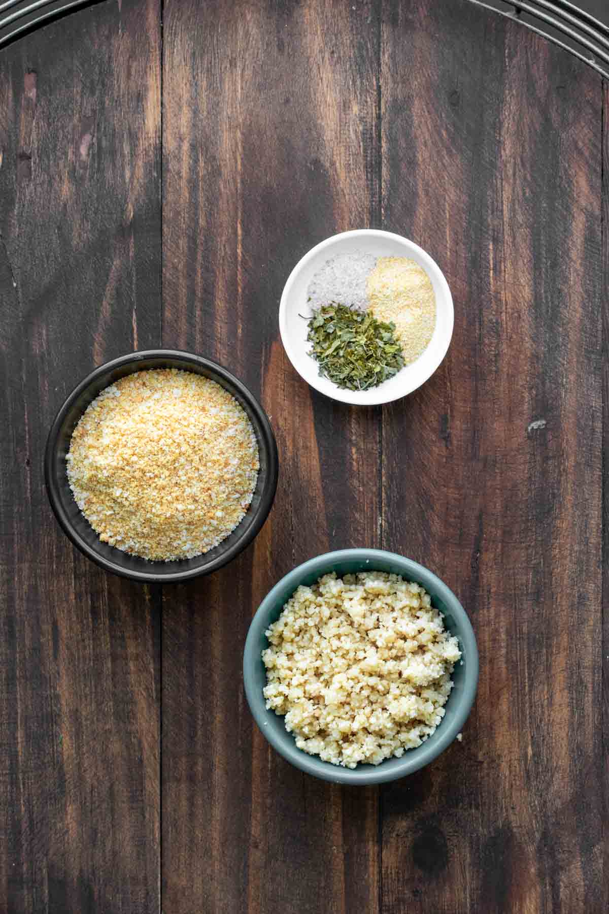 Bowls with ingredients needed to make a parmesan breadcrumb topping on a wooden surface.