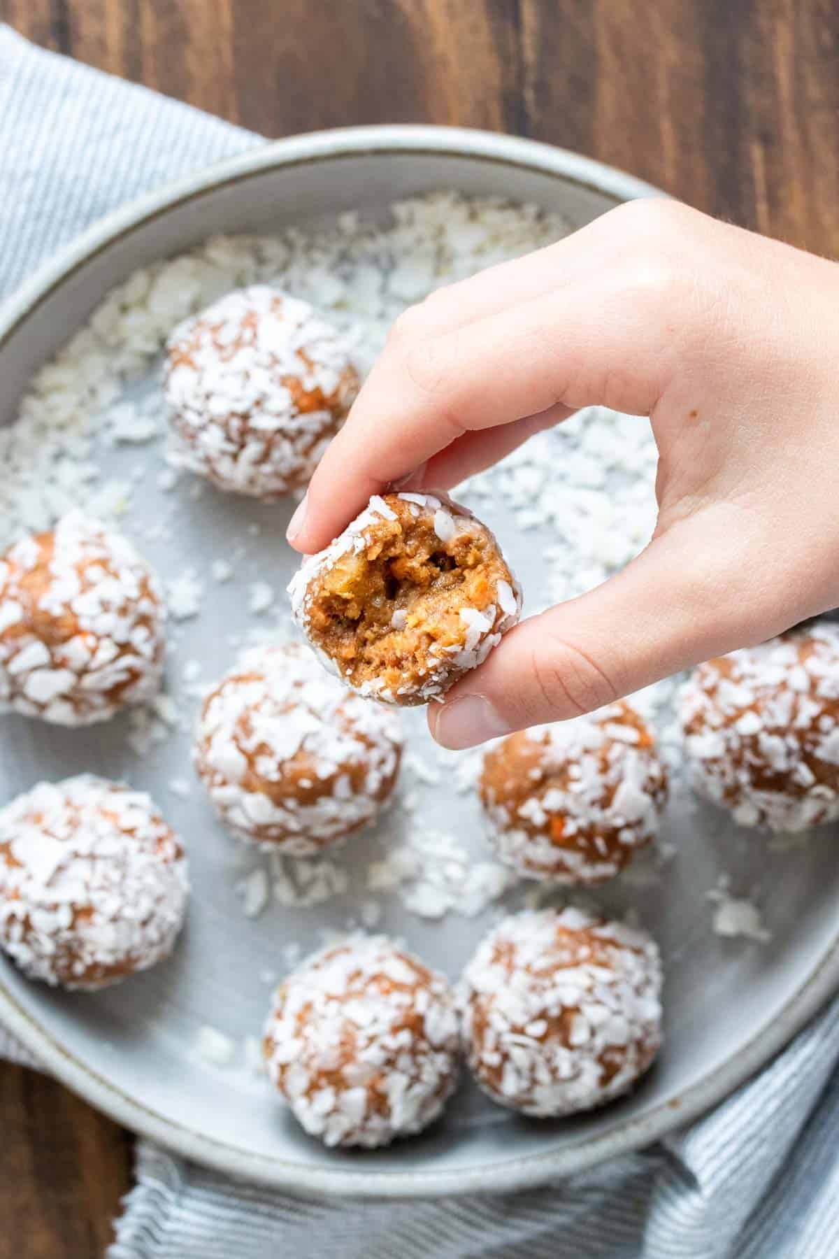 Hand holding a carrot cake energy ball with a bite out of it