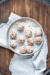 Carrot cake flavored energy bites coated in coconut laying on a grey plate on a wooden surface.