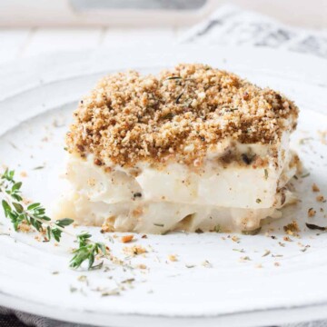 A close up shot of a slice of cauliflower casserole on a plate with a sprig of thyme