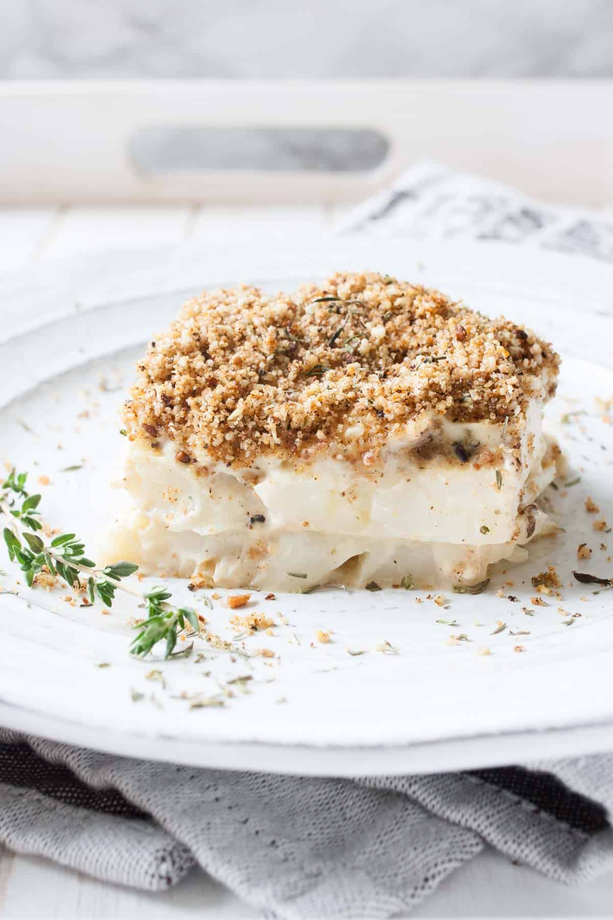 A close up shot of a slice of cauliflower casserole on a plate with a sprig of thyme