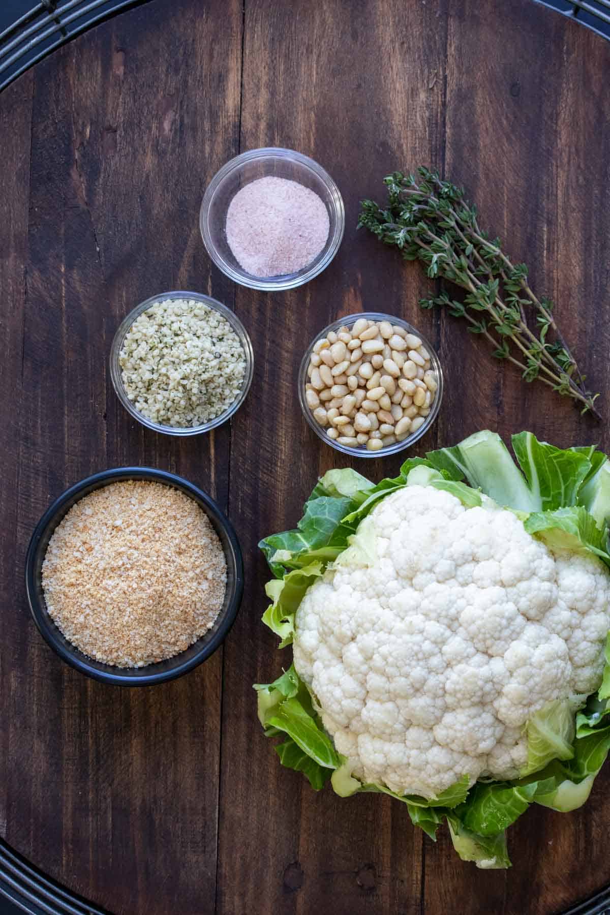 Cauliflower, bread crumbs, hemp seeds, pine nuts and salt on a wooden surface.